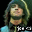Pixelated image of a person with long green hair and light skin, wearing dark clothing against black background.