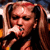 Static 50x50 pixel icon of a person with long brown hair in pigtails singing into a microphone, wearing dark clothing against a blurred background.