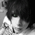 Black-and-white image of a person with dark hair and green eyes holding a small object near their face, displayed in a