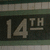 Static icon with "14TH" text on dark background, bordered by green and beige stripes.