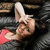 Pixelated image of a person with light skin and dark hair lying on their back, wearing a white headband and pink clothing against a dark background.
