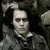 Pixelated grayscale image of a person with short dark hair wearing a dark jacket over a light collared shirt against a dark background.
