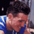 Pixelated static image of a person with dark hair wearing blue clothing, visible from the shoulders up against a dark background.