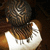 A person with braided hair wears a white sleeveless top with dark text on the back, viewed from behind against a dark background.