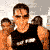 A person in a black sleeveless shirt with white text stands against a light background, performing sequential arm movements while wearing sunglasses.