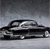 A static grayscale image of a classic sedan viewed from the side, positioned on a flat surface against a gradient background.