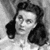 Black-and-white pixelated image of a person with dark hair styled in a side part, wearing a light-colored garment with a high collar.