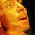 A pixelated close-up of a person's face with closed eyes, rendered in warm orange and yellow tones against a dark background.