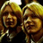 Two people with blonde hair appear in a pixelated image on a red background with orange text reading "How do you feel George?" and "Saintlike".