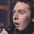 A 4-frame contact sheet of a person singing into a microphone with varying facial expressions and mouth positions across frames, displayed in a 2x2 grid layout on a gray background.