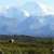 Pixelated landscape with blue sky, scattered clouds, and green-brown terrain under bright lighting.