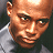 Pixelated close-up of a person's face with light brown skin tone, dark eyes, and a neutral expression, wearing a light-colored collared shirt against a dark background.