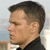 Pixelated profile view of a person with short dark hair wearing a dark high-collared shirt against a light background with blurred horizontal bands.