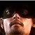Pixelated image of a person with light skin tone, dark hair, and a mustache, wearing a white shirt, holding a dark object near their face against a dark background.