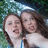 Two people with long brown hair pose closely together against a blurred green and blue background.
