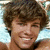 A pixelated image of a smiling person with brown curly hair, wearing light blue clothing against a yellow background with pink text.