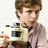 A person with light brown hair holds a beige digital camera, positioned against white and gray backgrounds displaying pixelated text.