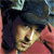 Pixelated close-up of a person with dark hair wearing a dark cap, light-colored shirt, and red garment, with a blurred background.