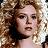 Pixelated close-up of a person with light brown curly hair, neutral expression, and visible neck against blurred background.