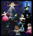 Static image of multiple characters from The Wizard of Oz in a theatrical stage performance with dark blue background and visible lighting effects.