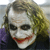 Static pixelated image of a person with white face paint, dark eye makeup, red lips, and messy brown hair, wearing a dark jacket over a purple shirt.
