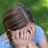 A pixelated image of a person with brown hair in a blue shirt covering their face with hands, set against a green background with blue text on a black field.