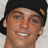 Pixelated close-up of a person wearing dark headwear with a small decorative element on the right side, set against a light background.
