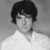 Black-and-white image of a person with dark curly hair wearing a white collared shirt against a gradient background.