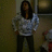 A pixelated static image shows a person with long dark hair wearing a light gray sweater and dark pants standing indoors.