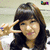 A person with long dark hair and bangs makes a peace sign, wearing a white top against a light background.