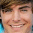 Pixelated portrait of a smiling person with brown hair and light blue clothing, next to blue text on black background.