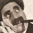 Pixelated grayscale image of a person with dark hair, mustache, and formal attire holding a dark object near the mouth.