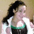 Pixelated image of a person with long dark hair in a ponytail wearing a white and green sleeveless top against a light brown background.