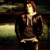 Pixelated image of a person with light brown hair wearing dark clothing, standing against a blurred background with green and yellow tones.