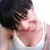 Pixelated close-up of a person with dark hair and light skin wearing a white top, cropped to show only the upper face and shoulders.