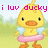 Pixelated yellow duck with orange beak and feet, wearing light blue wings and pink tutu, standing on green grass with light blue sky background, text 'i luv ducky' in pink above.