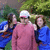 A group of people in outdoor setting with greenery, one person wearing pink sweater and white cap, others in blue clothing.