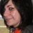 Pixelated close-up of a person's face with dark hair, light skin, and a neutral expression against a dark background with a red garment visible.
