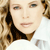 A pixelated close-up of a person with light brown hair, wearing a white top, and a dark accessory near the neck.