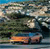 A pixelated static image shows a vehicle with a bright orange section on a road, surrounded by blurred greenery and sky.
