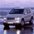 Pixelated image of a light gray van with dark windows and black wheels, positioned on a reflective surface under a gradient sky.
