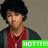 Pixelated image of a person with dark curly hair wearing red and gray clothing, standing against a neutral background with green text overlay.