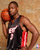 Pixelated image of a basketball player in dark jersey holding orange ball, standing against light brown background with red and white elements.