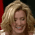 A pixelated close-up of a person with light brown curly hair, smiling with visible teeth, against a dark background with red and white elements.