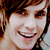 Pixelated close-up of a smiling person with brown hair and light skin, cropped to show face and upper shoulders.