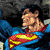 Static pixelated image of a cartoon character in blue and red costume with yellow emblem, facing left against dark background.