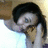 Pixelated static image of a person with dark hair, light skin, and a white shirt, holding a light brown object near their face against a gradient background.