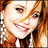 A pixelated close-up of a smiling person with light brown hair, wearing a dark jacket over a white shirt.