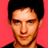Static pixelated image of a person with short dark hair against a solid pink background, wearing a black top.