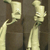 Two pixelated light-colored figures with elongated necks and rounded heads stand side-by-side against a dark brown background.